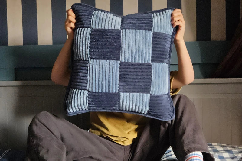 A blue corduroy Check Cushion held in front of a child.