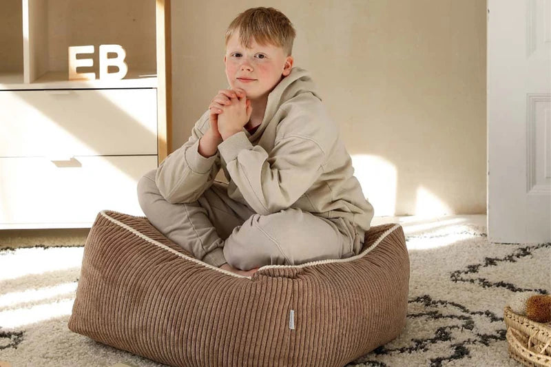 Ein Kind sitzt auf einem braunen Kumo Ottoman aus Cord.