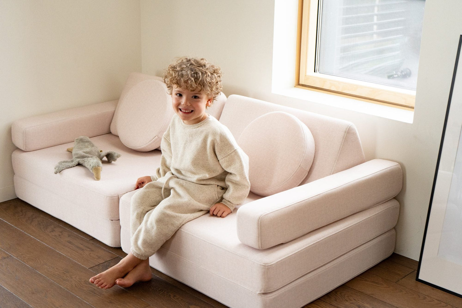 Boy sitting on the arm of a light pink play sofa by a window