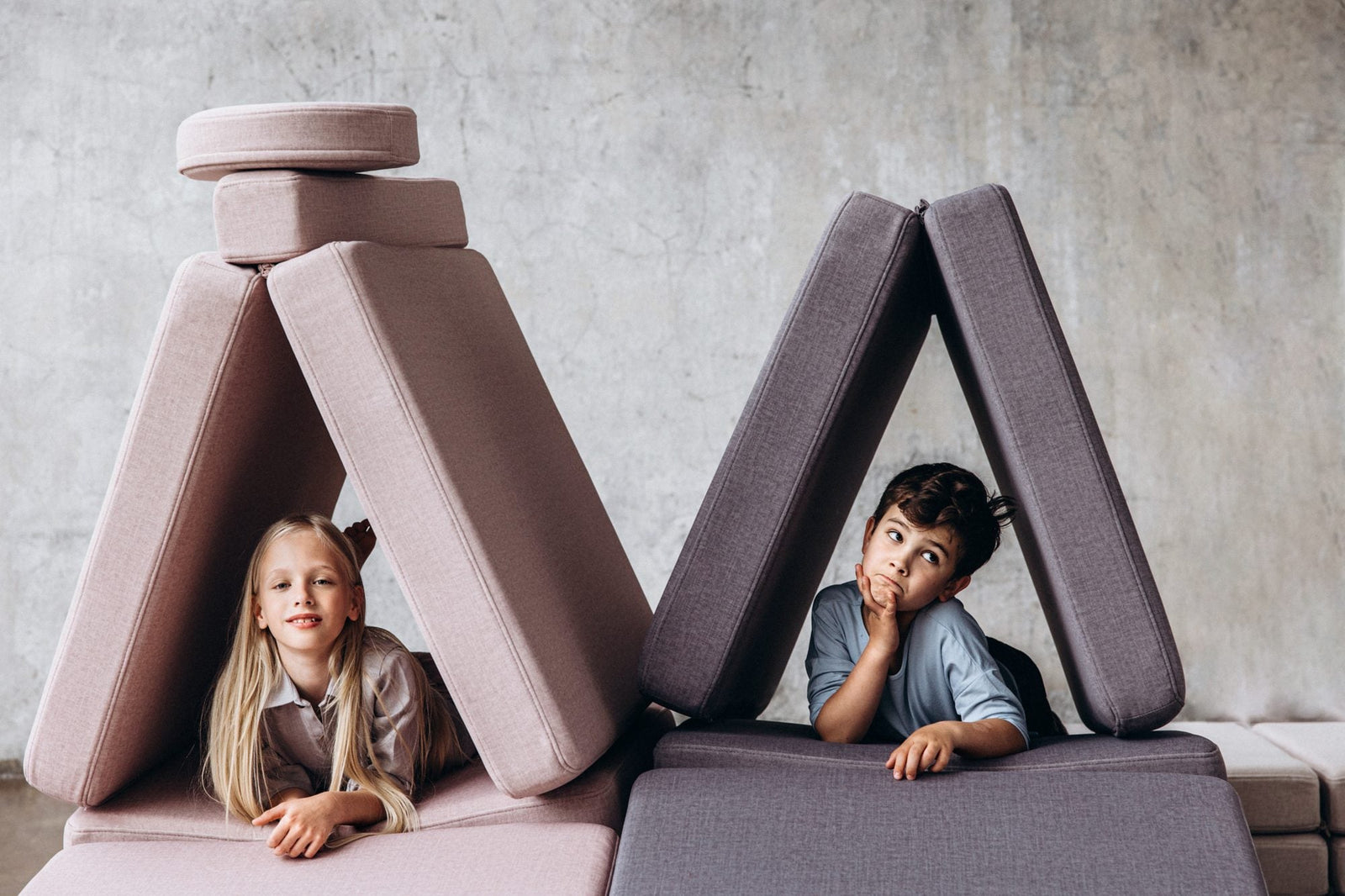 Girl and boy lying in two tents built from pink and grey play sofa cushions