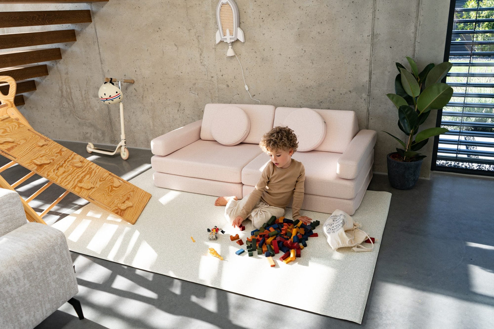 Light pink play sofa in a bright living room with a boy playing with wooden blocks