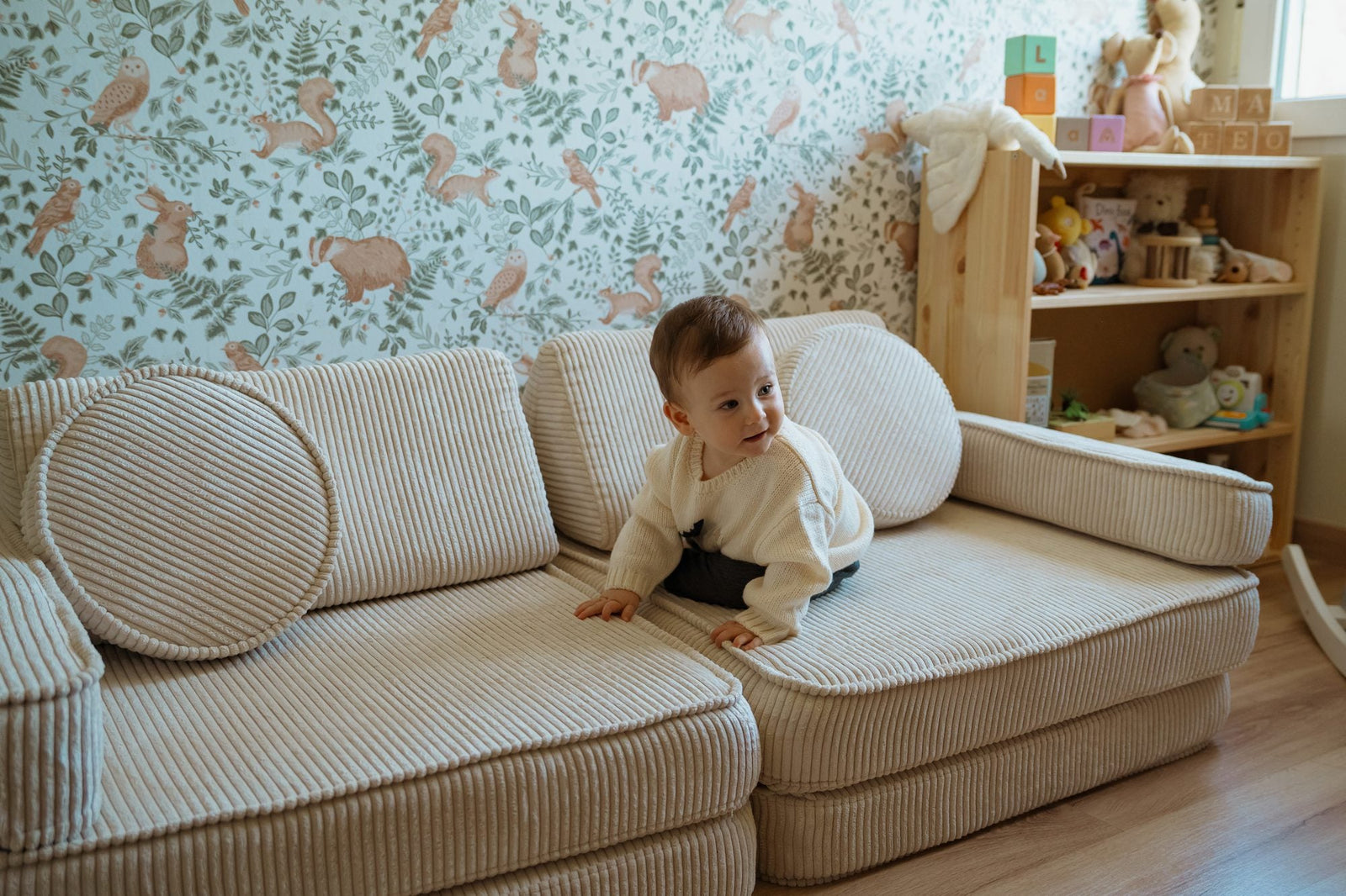 Toddler on a cream corduroy play sofa in front of woodland-print wallpaper