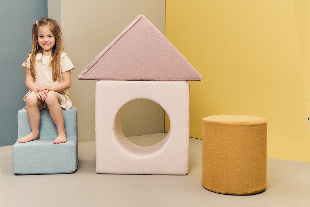 Girl sitting on the steps next to a house built from the cube and slide