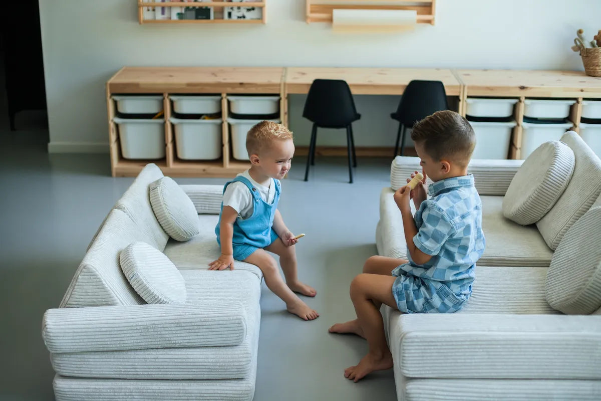 Twee jongens zitten tegenover elkaar: links op de Speelbank Mini, rechts op de grote Speelbank, beide van Corduroy