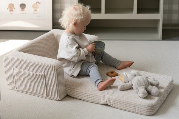 Child sitting on an unfolded cream corduroy Lumi Chair.