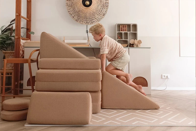 Child climbing a beige Slide beside stacked play sofa modules.