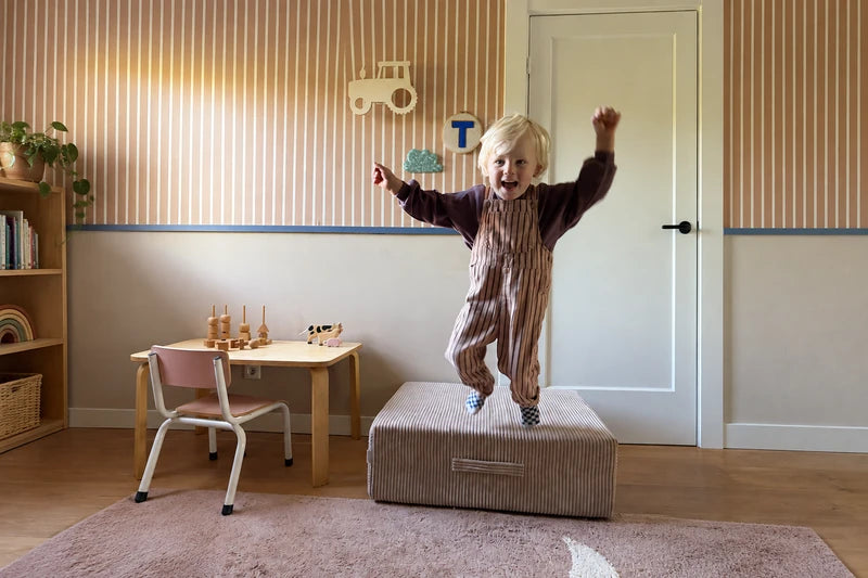 Child jumping on a corduroy Trampoline in a playroom.