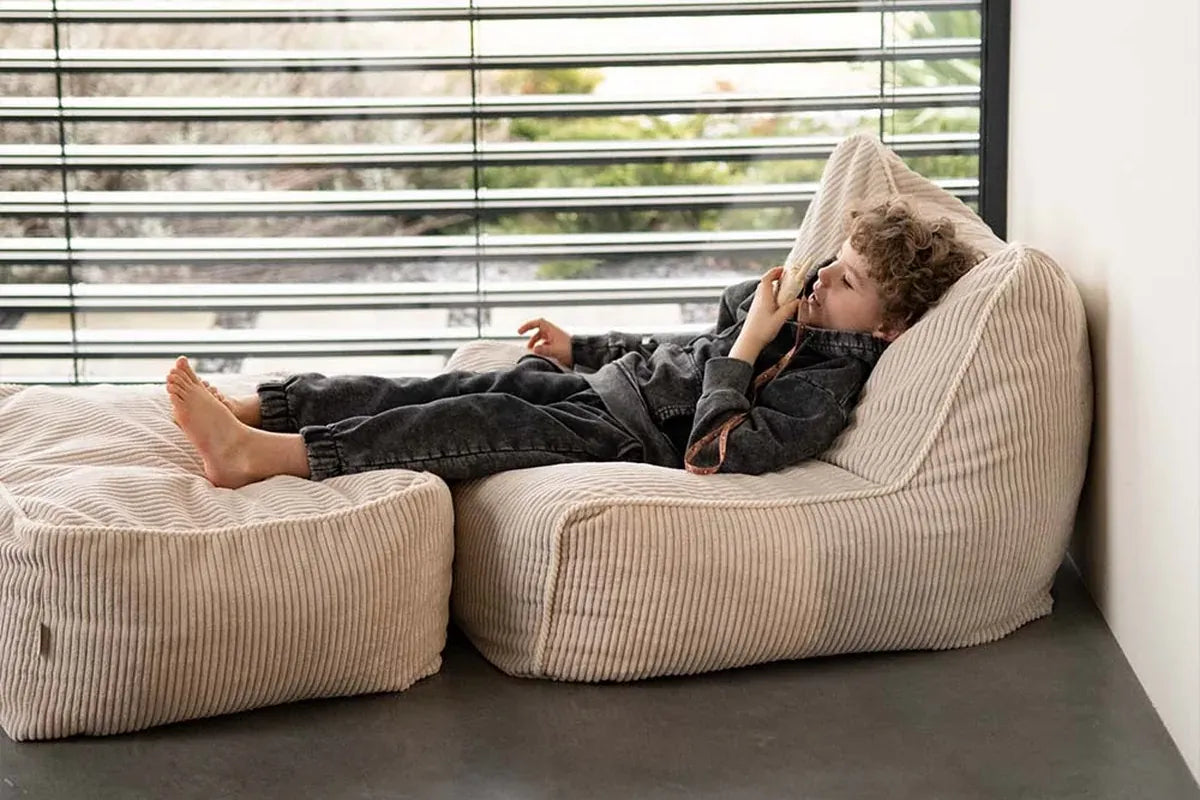 Boy resting on Kumo Chair and Ottoman in Vanilla by a window