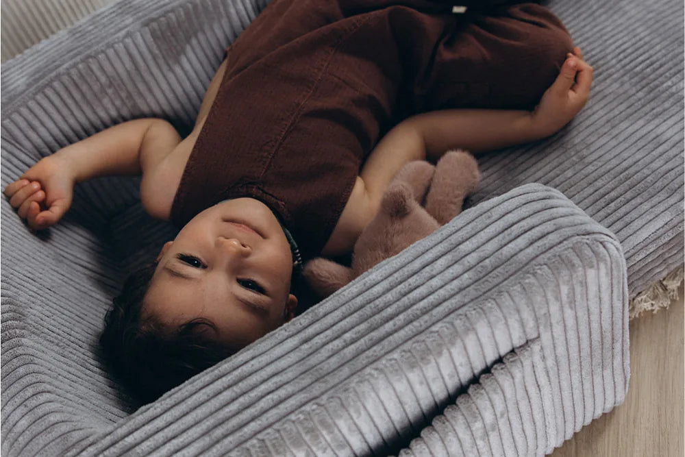 Child resting on Lumi Chair Corduroy in Pebble, unfolded