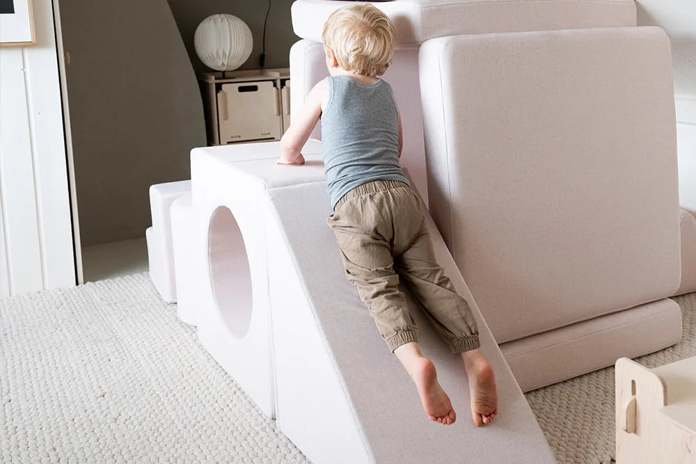 Child climbing up the slide of a Playset build in a room under the roof