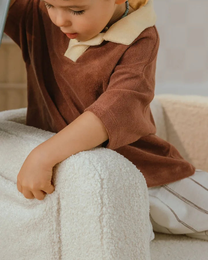 Child sitting on Lumi Chair Teddy in Soft Cream with a book
