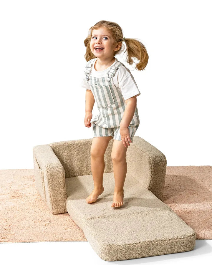 Girl standing on Lumi Chair Teddy in Light Beige, unfolded