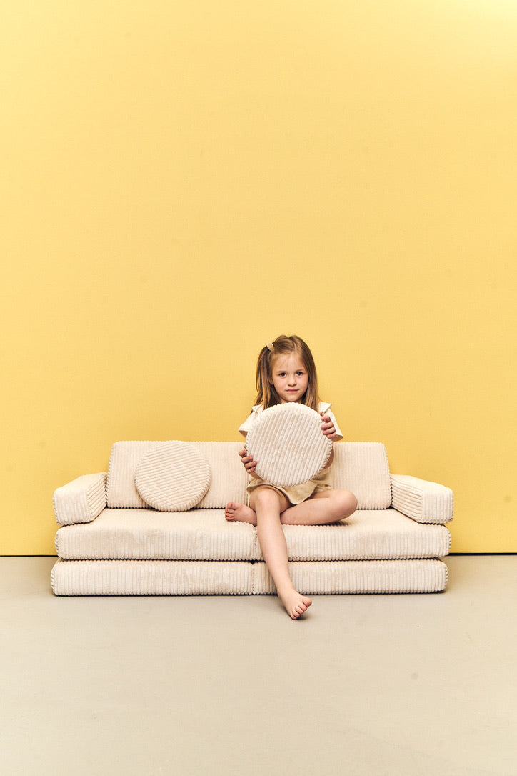 Child sitting on Play Sofa Pure Corduroy Mini in Vanilla with a round cushion
