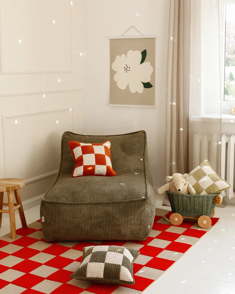 Kumo Lounger coloris Dusty Sage dans une chambre d’enfant, sur un tapis à carreaux rouges et blancs