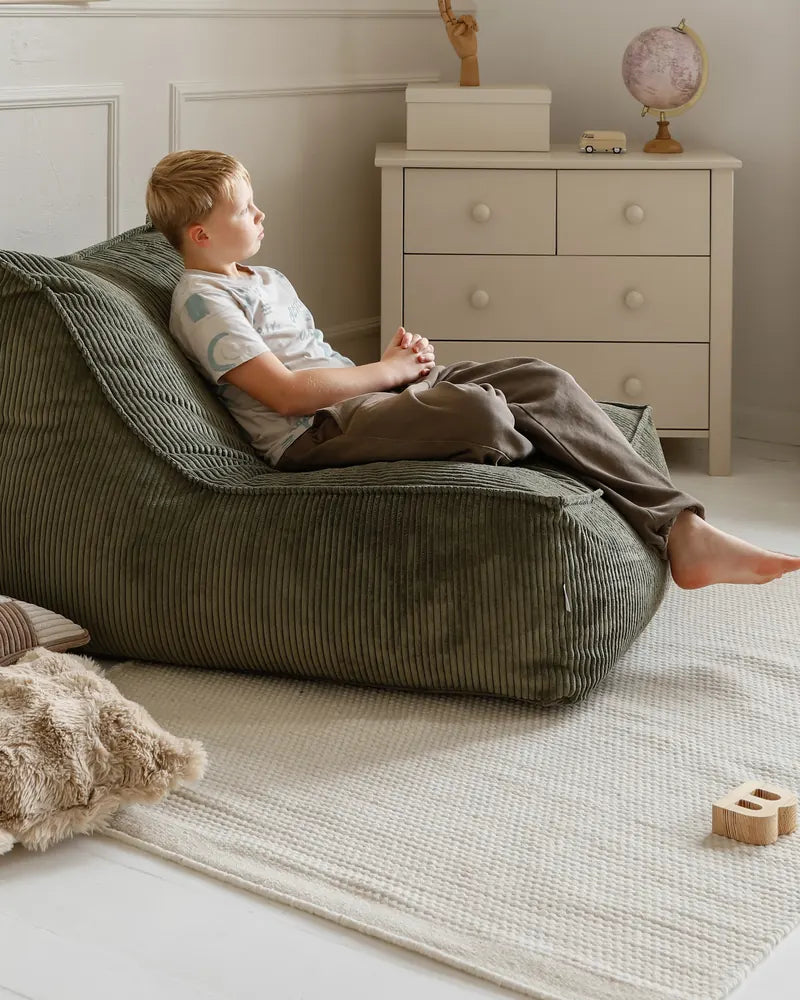 Un garçon confortablement allongé dans le Kumo Lounger, le fauteuil entier visible dans la pièce