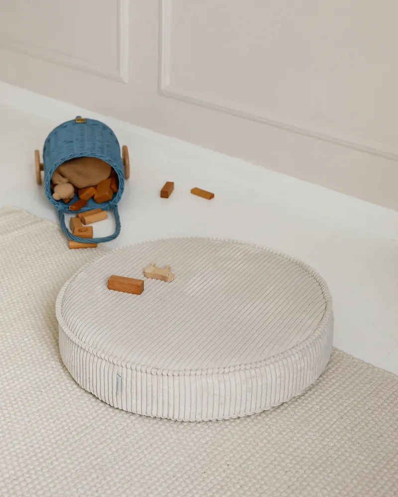 Yuka Pouf in Vanilla on a rug next to wooden toys