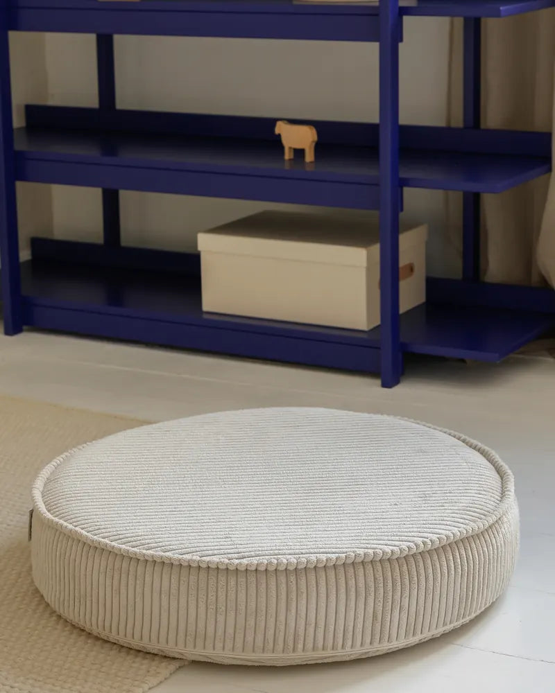 Yuka Pouf in Vanilla in front of a shelf